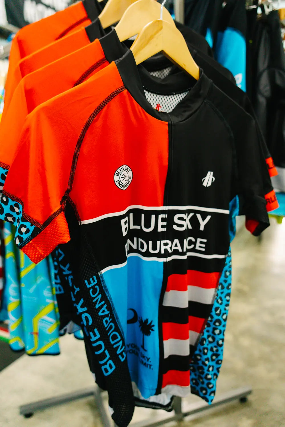 Custom Blue Sky Endurance cycling jerseys in red, blue and black on hangers