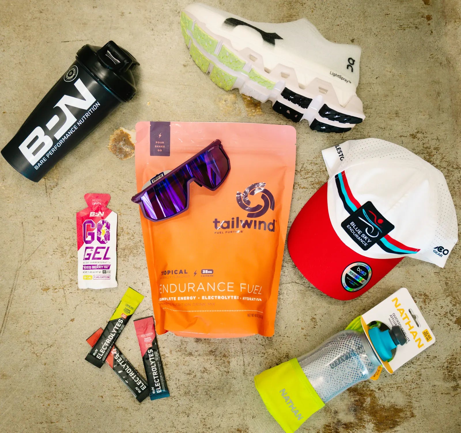 Race-day essentials including Tailwind Endurance Fuel, GU gels, sunglasses, a running cap, On shoes and a shaker bottle