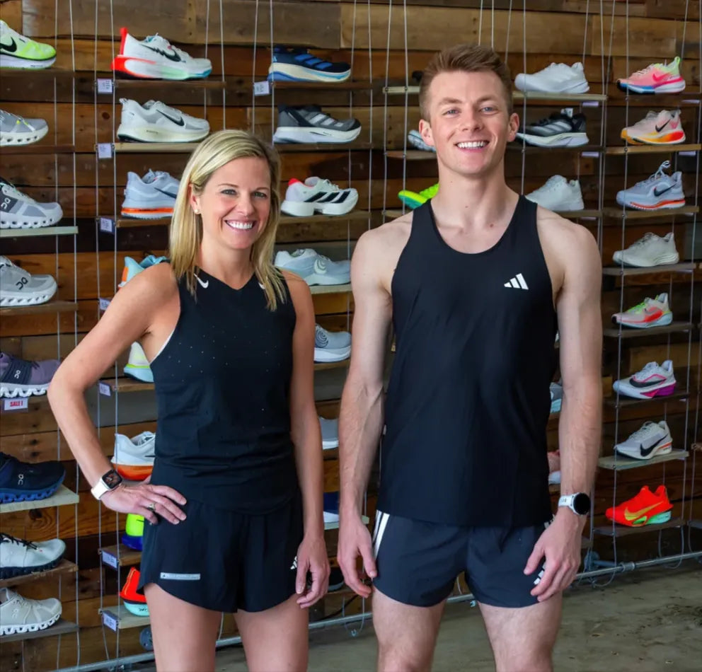 Two runners in Blue Sky Endurance gear standing in front of the running shoe wall